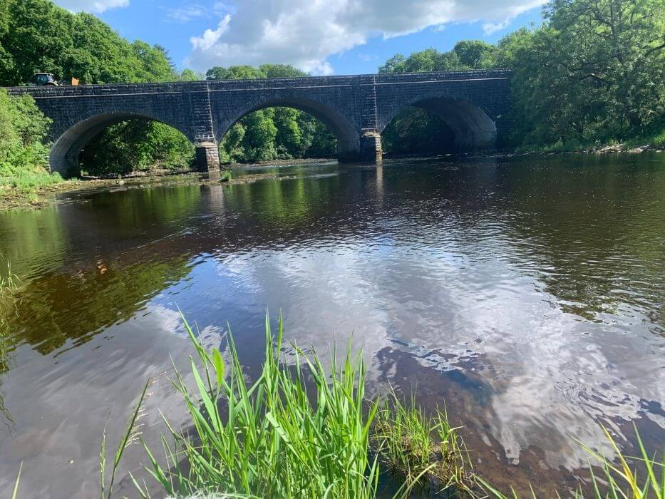 The new bridge of Dee - that carries the A75 - from the river view. The clouds and bridge are reflected in the river. The sides of the bridge are detailed stone in contrast to the A-road that runs over it.